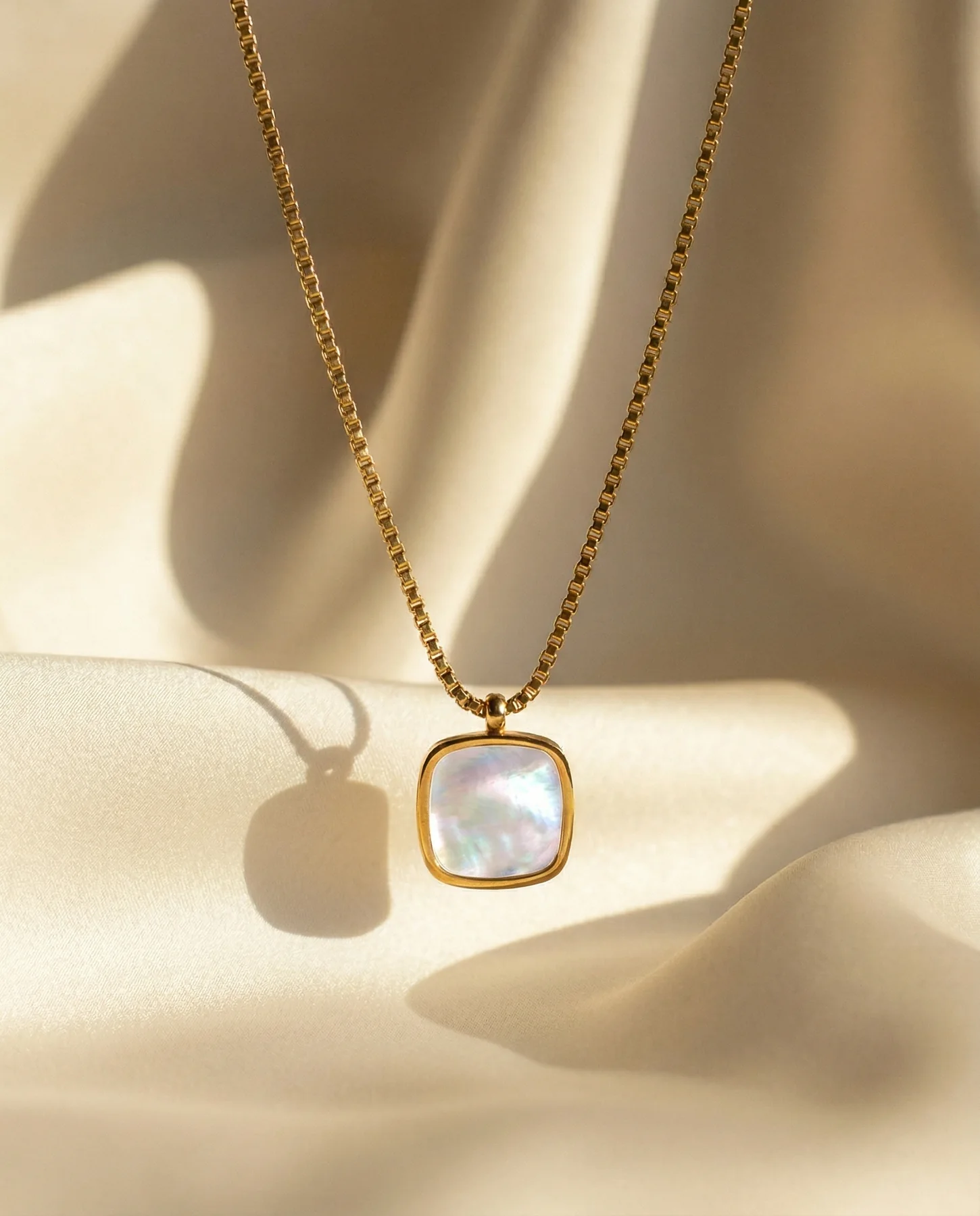 Gold pendant photographed on softly lit ivory fabric for B Classy
